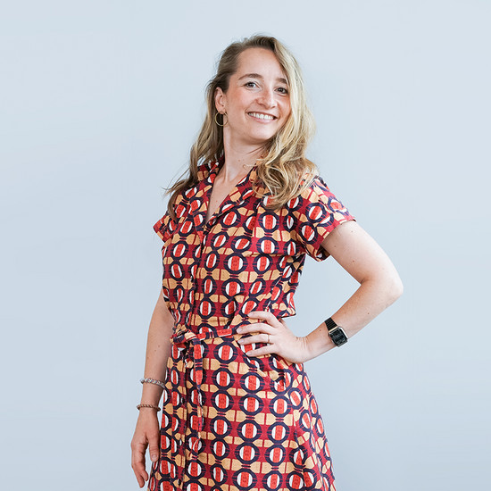 Eine Frau mit einem rot schwarzem kleid und angewinkeltem Arm. Sie lächelt selbstbewusst in die Kamera.