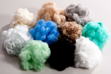 Mucchi di cotone colorato in varie tonalità, disposti su uno sfondo bianco.