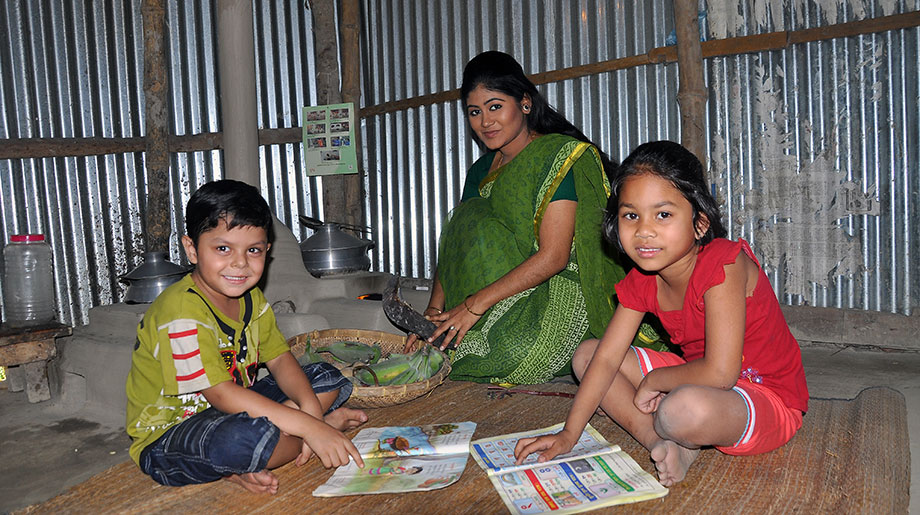 A woman and her two children sit on the ground and are posing for the picture with reading material.