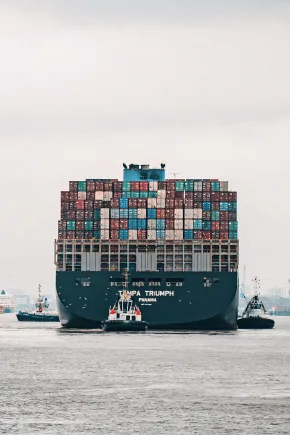 The picture shows a large container ship travelling on a river from behind