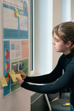 A pupil sticks small pieces of paper on a board with diagrams and pictures.