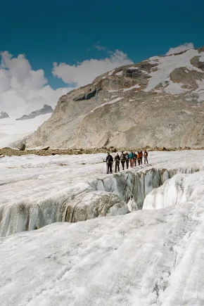 Eine Gruppe von Menschen geht gemeinsam über eine alpine Gletscherlandschaft.