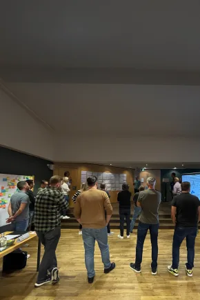 Eine Gruppe von Personen steht in einem Workshopraum vor einer Präsentation.